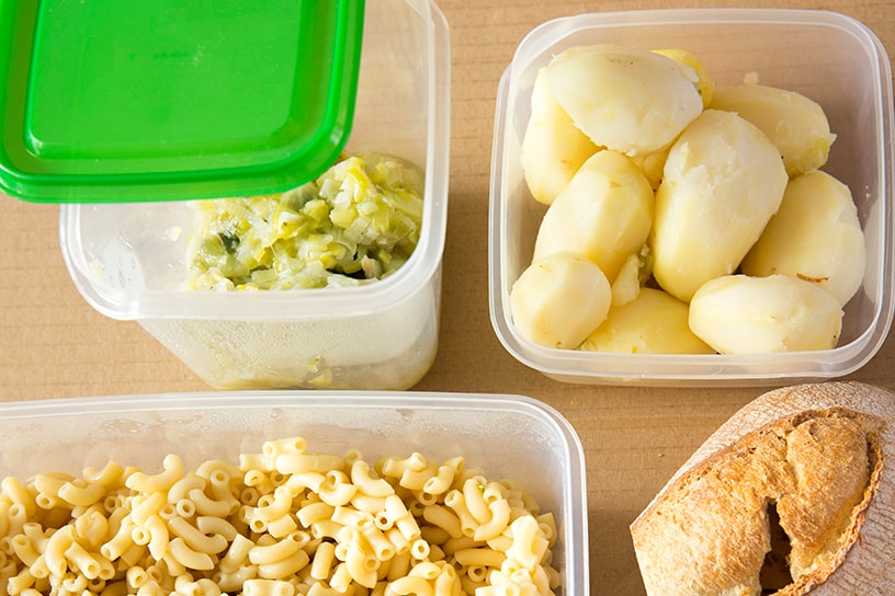 Een bakje met gekookte aardappelen, een bakje met gekookte pasta, een bakje met groenten en een stuk brood